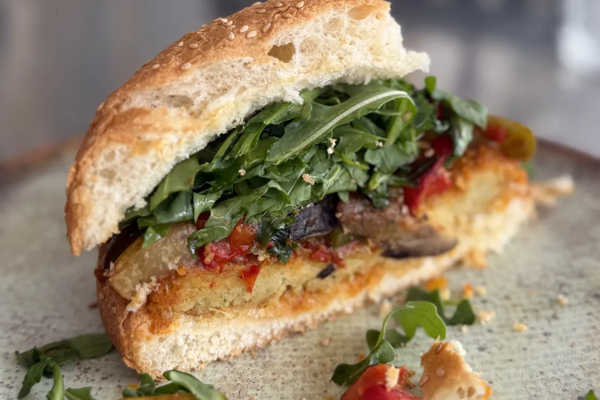 Hamburguesa vegetariana con verduras asadas, r&uacute;cula y salsa de tomate en pan de semillas