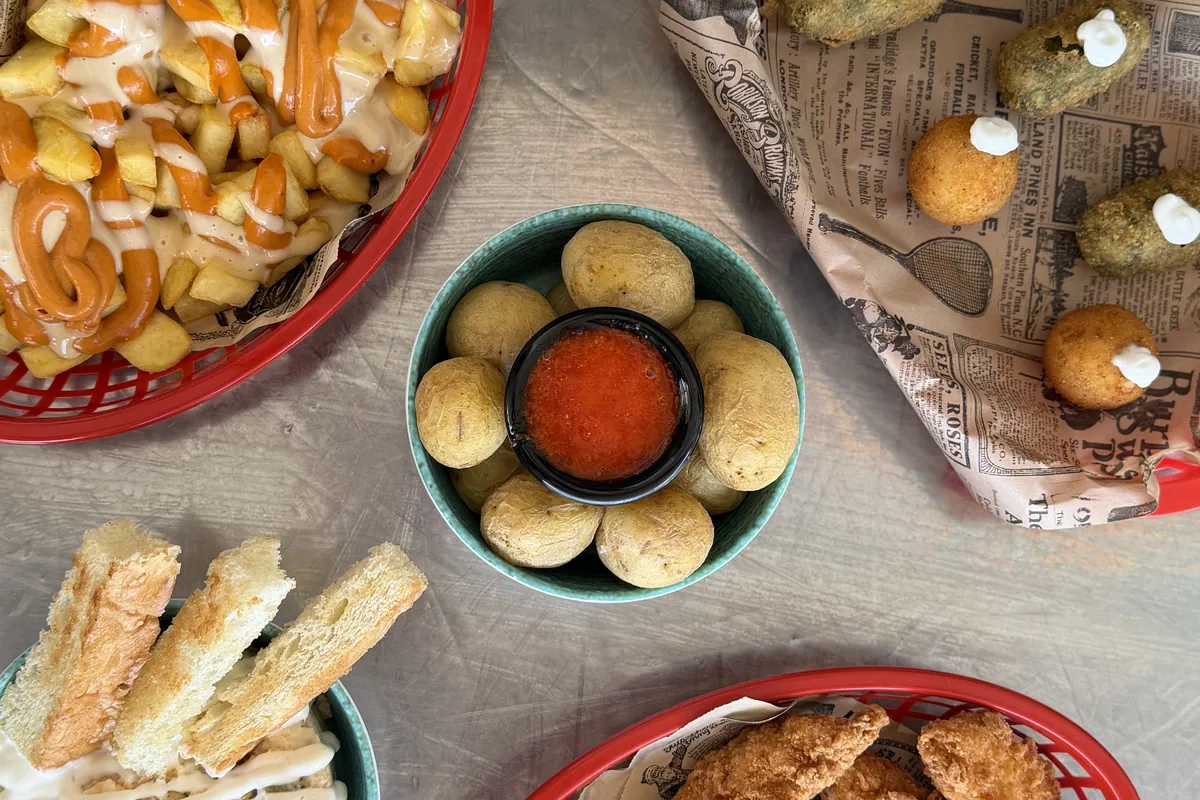 Vista cenital de varios entrantes: patatas con salsa, croquetas, jalape&ntilde;os rebozados y tiras de pollo frito con sus salsas